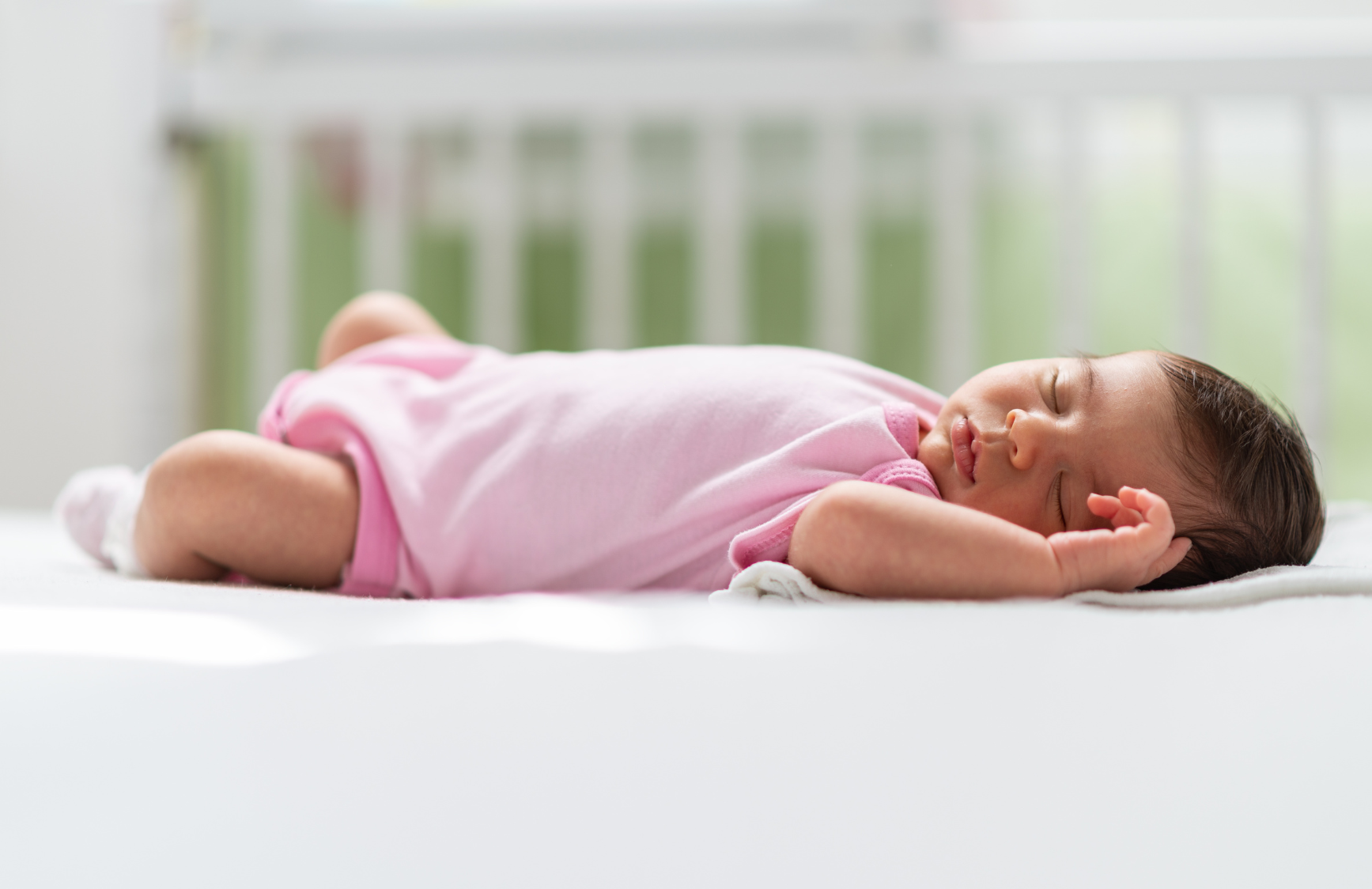 A baby sleeping in a crib on their back. There are no other items in the bed with the peacefully-sleeping infant